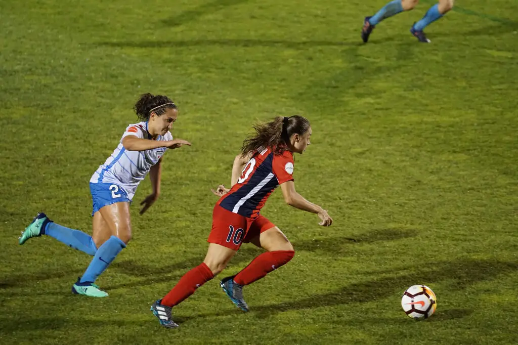 Two woman playing soccer on green field