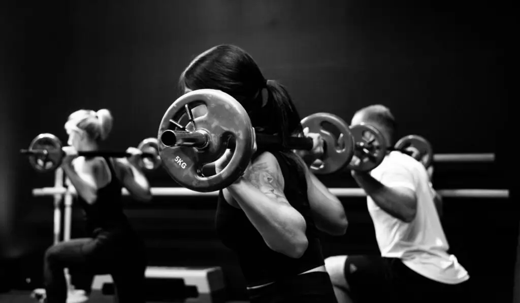 Black and white photo of a woman lifting a barbell from a squat position Featured image for Importance of Progressive Overload blog for Pivotal Motion Physiotherapy.